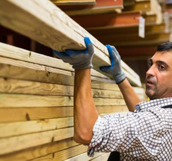 A man is holding a wooden beam in a warehouse.